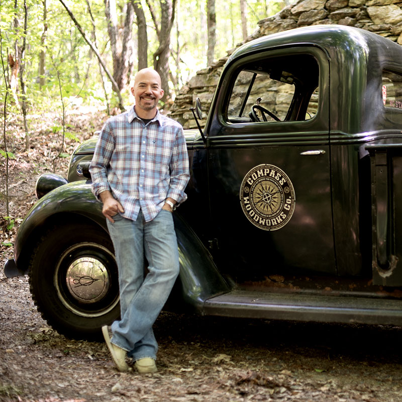 Brad Taylor, owner of Compass Woodworks, leaning against his 1939 pickup out in the woods.
